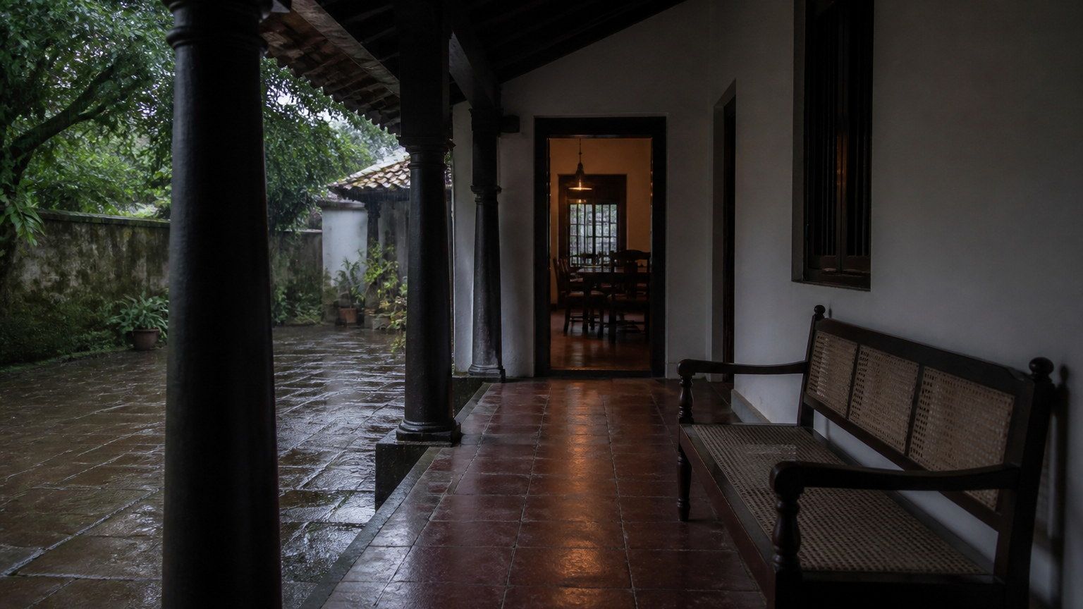 Indian residential threshold in monsoon light, with wet stone outside and a protected interior beyond