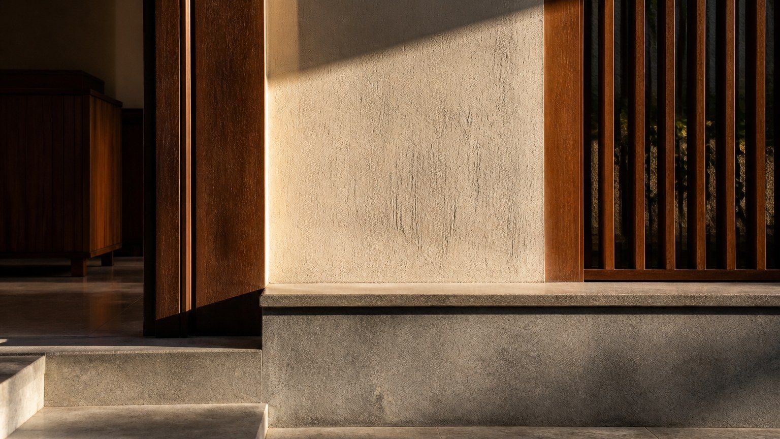 Honed stone, timber and textured plaster receiving sharp side-light in a contemporary Indian interior