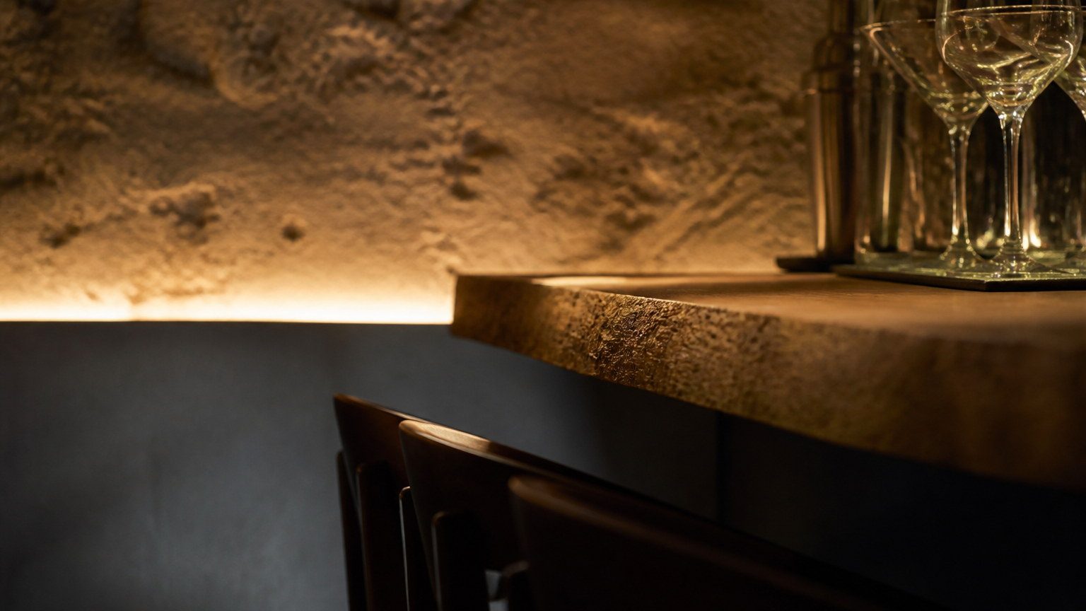 Hospitality material detail: a stone counter edge with warm concealed lighting grazing a textured wall