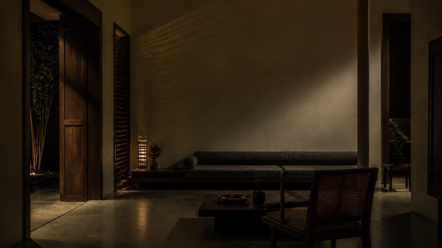 Evening in a restrained Indian home with spare artificial light and a calm empty wall
