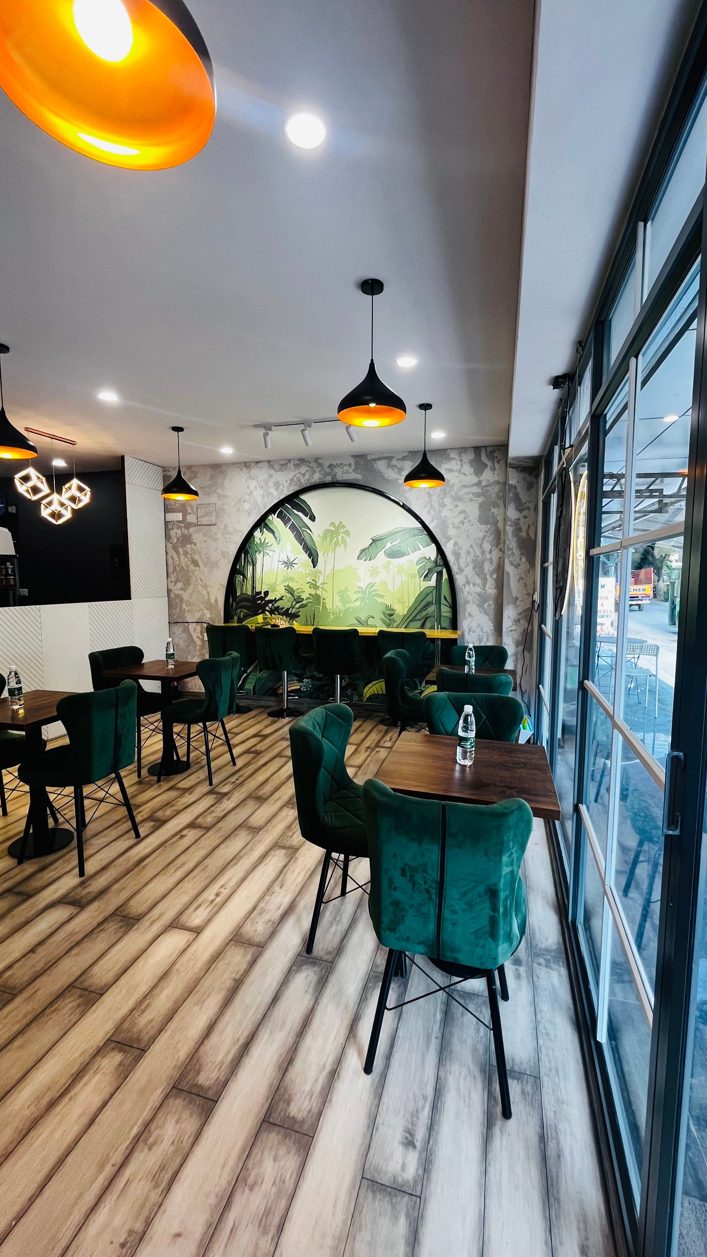 Café dining at Amaiga with green velvet seating, tropical mural and street-facing glazing