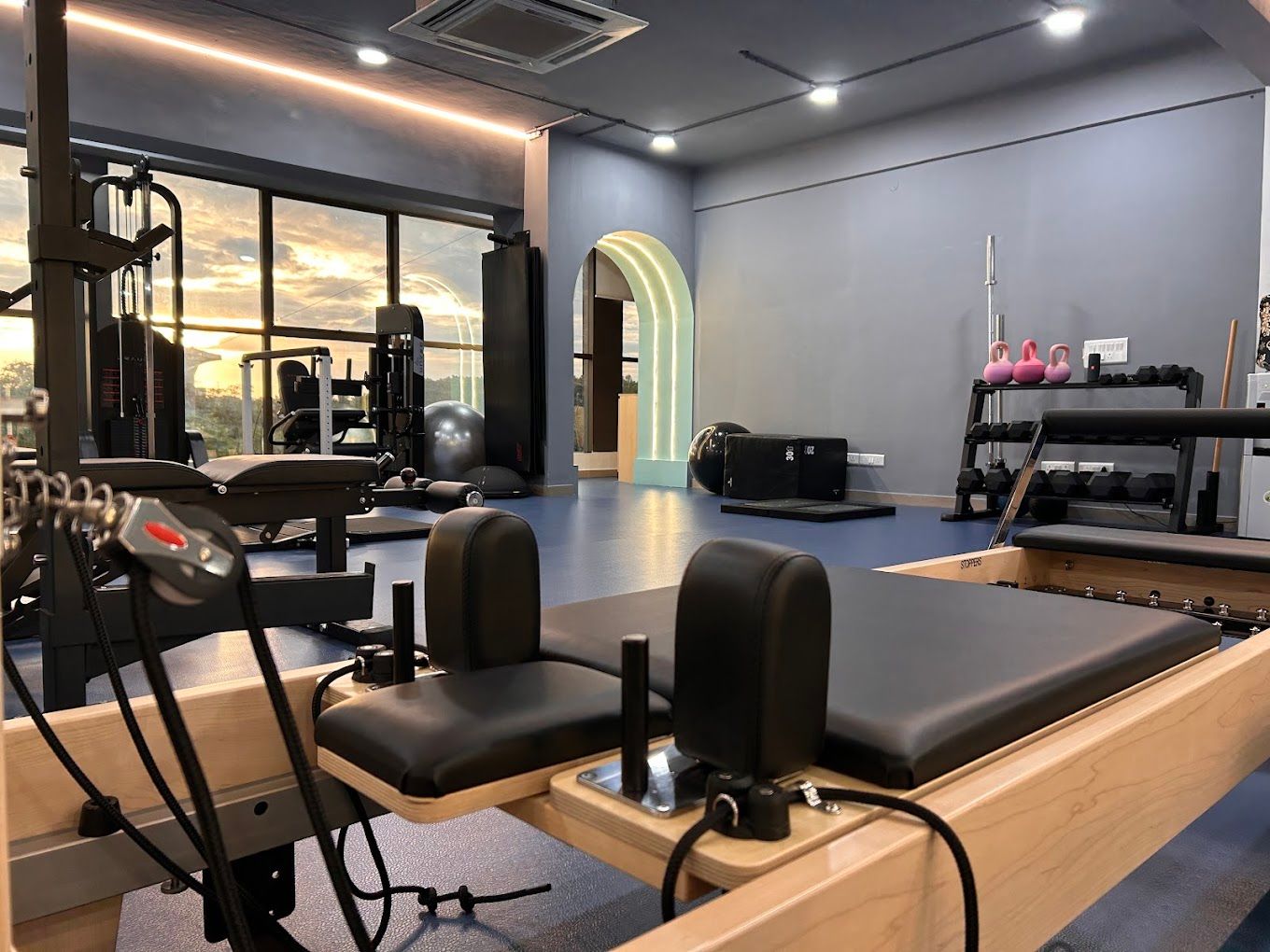 Wooden reformer facing an illuminated arch and dumbbell rack