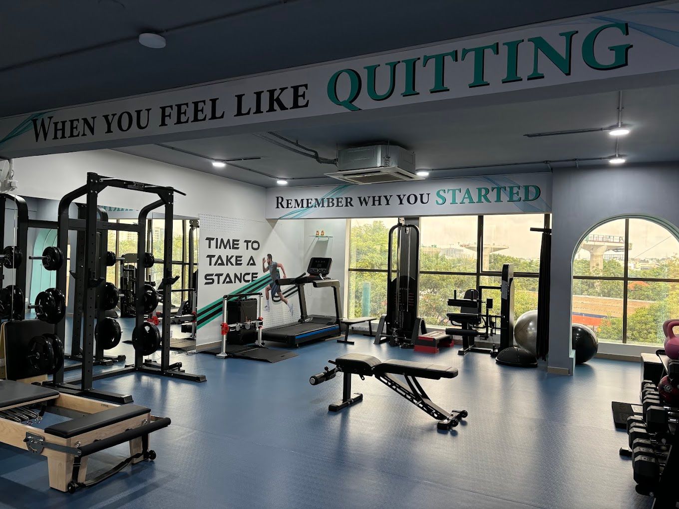 Gym with blue rubber flooring, reformer, racks, and wall lettering