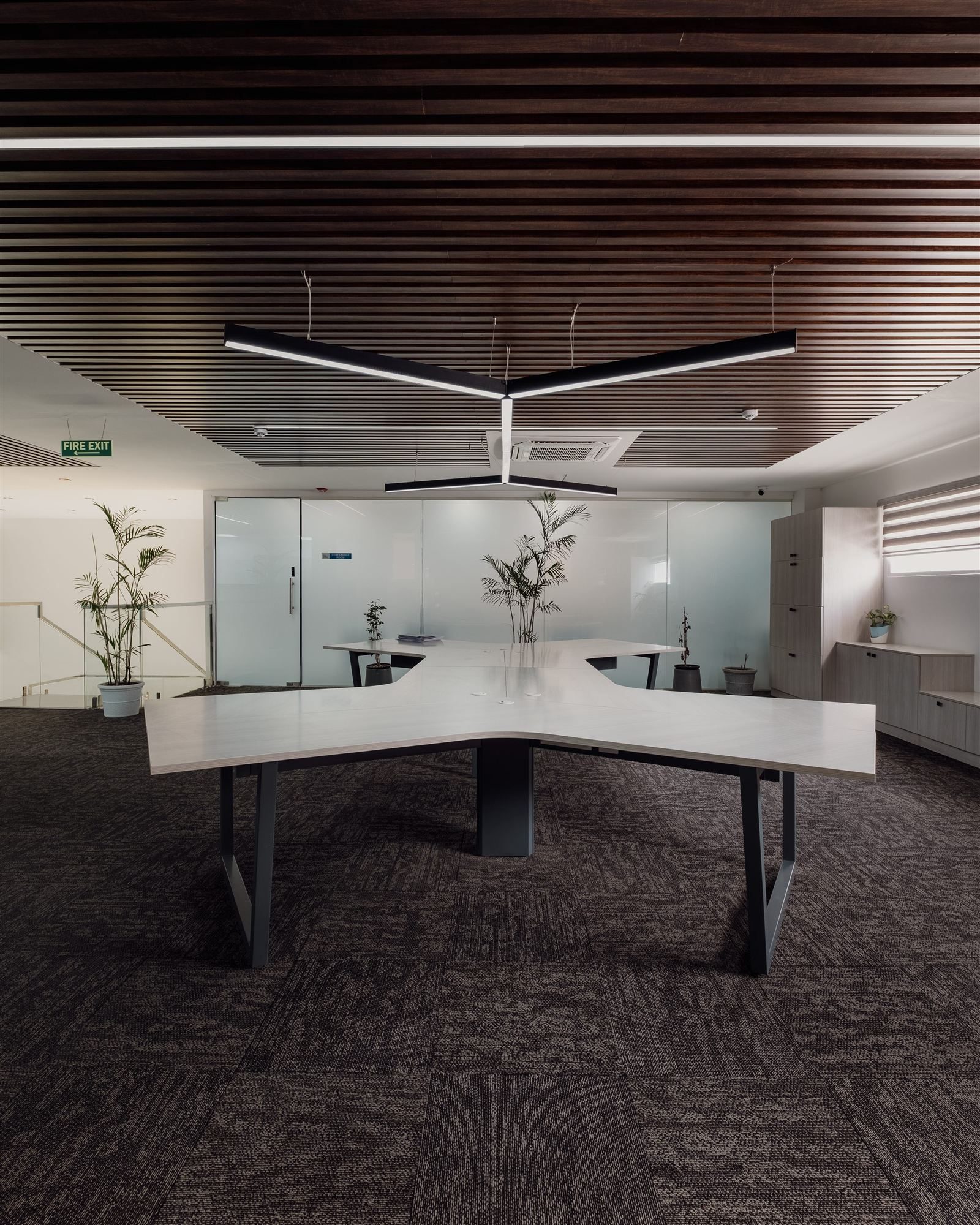 Sculptural X-shaped workstation cluster beneath a dark slatted wood ceiling