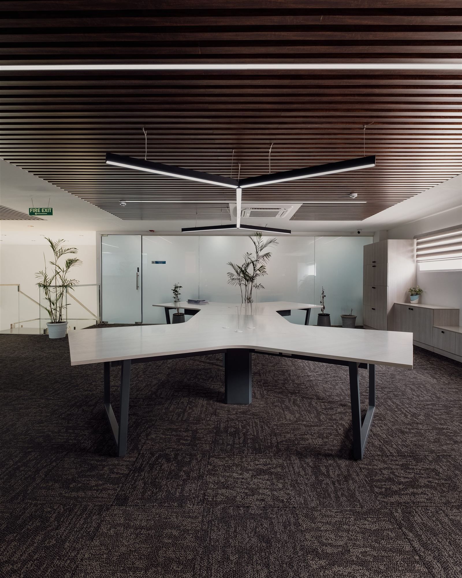 Sculptural X-shaped workstation cluster beneath a dark slatted wood ceiling